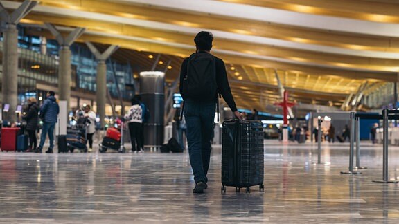 Touristen mit Rucksack und rollenden Koffern in einer Halle eines Flughafens.
