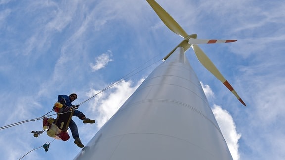 Ein Industriekletterer hängt neben dem Mast einer Windenergieanlage