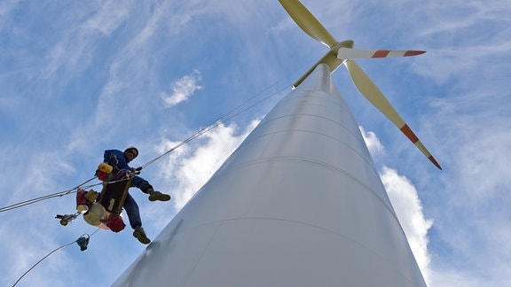 Ein Industriekletterer hängt neben dem Mast einer Windenergieanlage