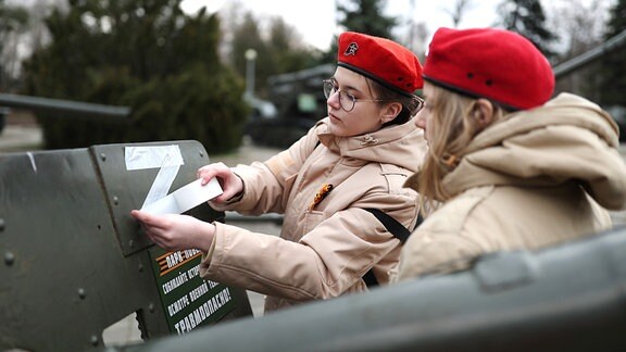 Eine junge Frau klebt ein weißes Z-Symbol auf ein Armeefahrzeug