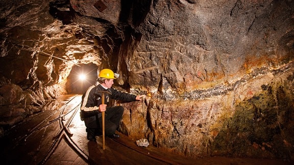 Ein Bergwerksführer präsentiert im Besucherbergwerk Vereinigt Zwitterfeld zu Zinnwald eine Stufe des Minerals Zinnwaldit