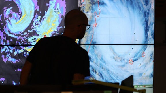 Ein Meteorologe steht vor Monitoren, die den Wirbelsturm "Belal" zeigen