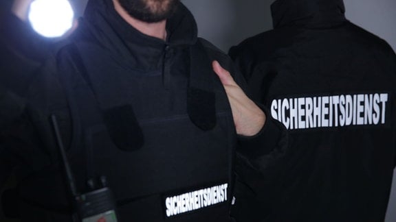 Im Bild sind zwei Männer mit dunkelblauer Sicherheitsweste und Taschenlampe ohne Gesicht zu zeigen, zu sehen.