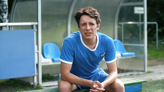 Ein Fußballspieler in einem blauen Trikot sitzt auf einer Bank.