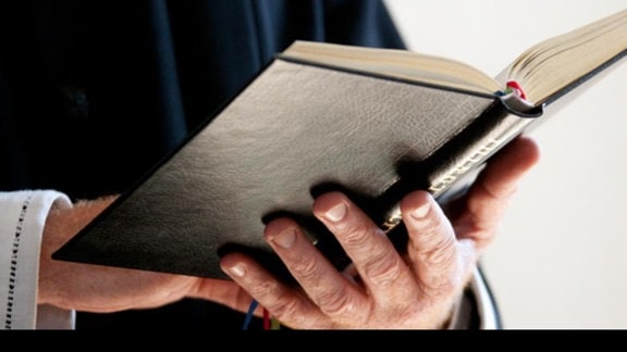 Ein Priester hält ein aufgeschlagenes Buch in den Händen.