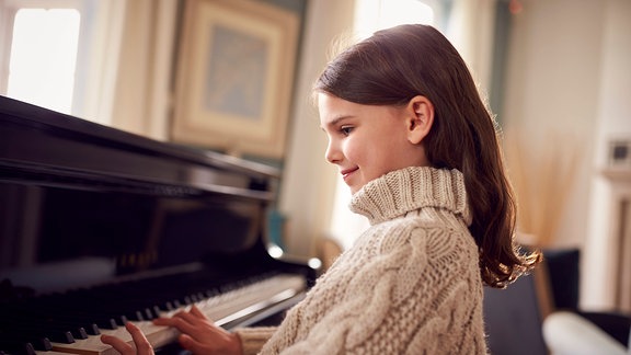 ein Lehrer übt mit einem kleinen Mädchen Klavierspiel.
