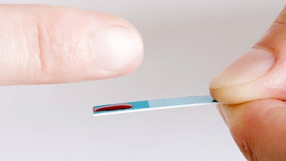 Ein Blutstropfen aus einem Finger auf einem Teststreifen.