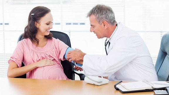 Arzt misst Blutdruck bei einer schwangeren Patientin