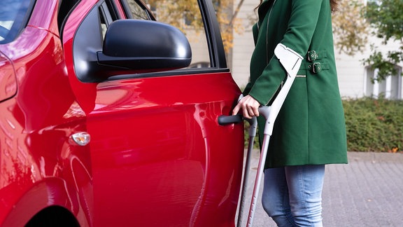 Eine Frau mit Krücken, die eine Tür eines Autos öffnet