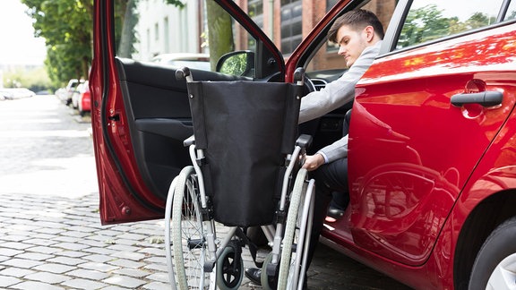 Ein Mann, der im Auto sitzt und seinen Rollstuhl faltet