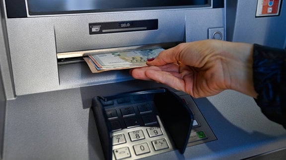 Eine Frau zieht 100 EURO Bargeld am Geldautomat.