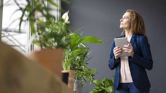 Frau steht neben einem Fensterbrett voller Pflanzen