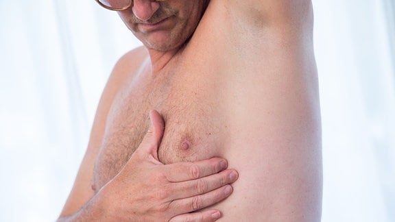 Ein Mann betastet seine Brust.