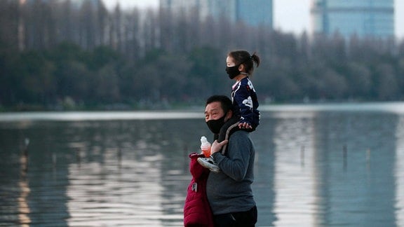 Ein Vater geht mit seiner Tochter am Ufer des Jiangsu-Flusses in der chinesischen Stadt Nanjing entlang. Bei tragen einen Mundschutz.