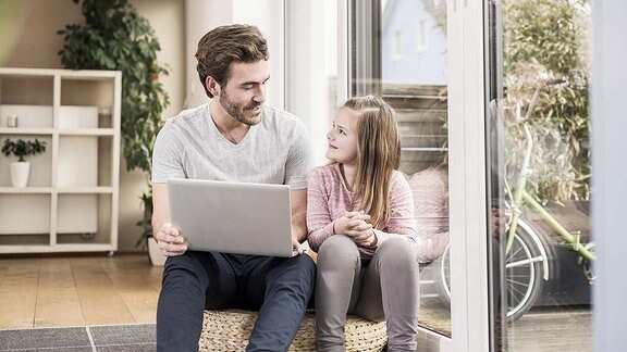 Ein Vater sitzt mit seiner Tochter am Laptop.