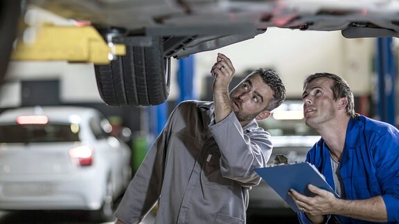 Zwei Automechaniker in einer Werkstatt, die gemeinsam das Auto untersuchen.