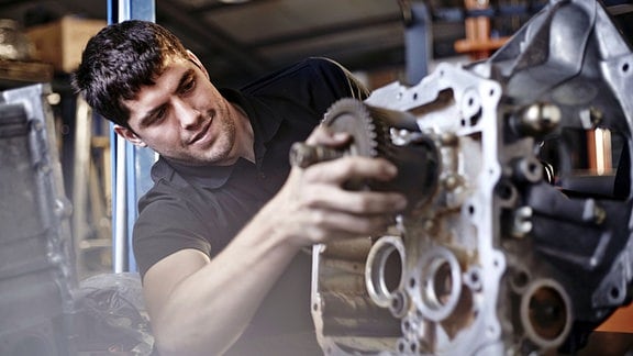 Ein Kfz-Mechaniker arbeitet an einem ausgebauten Motor.
