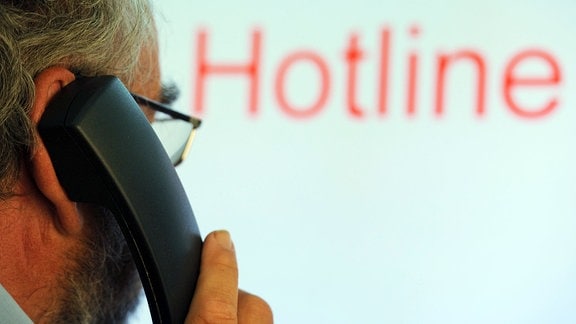 Illustration: Ein Mann hält einen Telefonhörer vor den Schriftzug «Hotline» auf einem Computermonitor.
