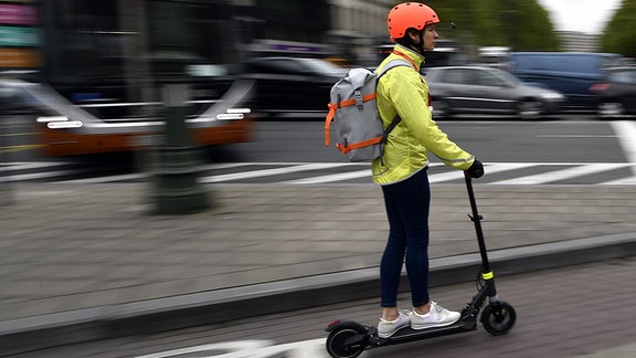 Ein Frau fährt auf einem E-Tretroller auf einem Fahrradweg.