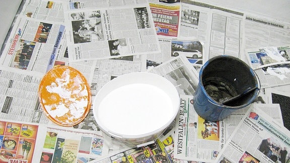 Farbeimer mit weißer und schwarzer Farbe stehen auf ausgelegtem Zeitungspapier.