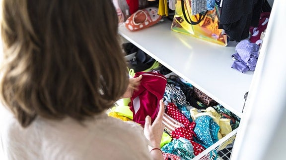 Eine Frau vor einem geöffneten Kleiderschrank hat ein Kleidungsstück in Händen