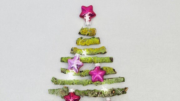 Äste mit Moos in Weihnachtsbaum Form an Wand mit Dekokugeln. 