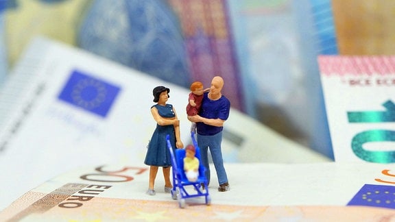 Themenbild - Plastikfiguren zeigen eine junge Familie mit Kinderwagen auf Euro Banknoten stehend.