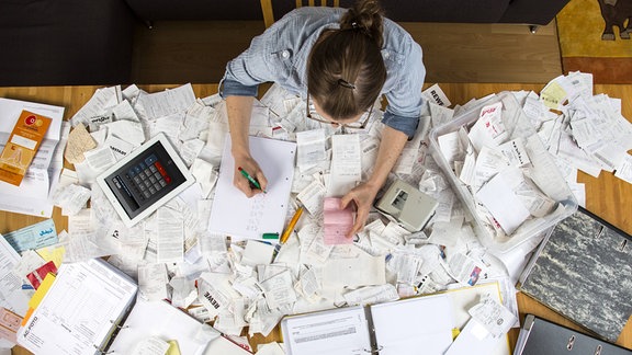 Junge Frau sortiert zuhause, am Schreibtisch, diverse Belege, Unterlagen, Rechnungen und Kassenbons für die Steuererklärung.