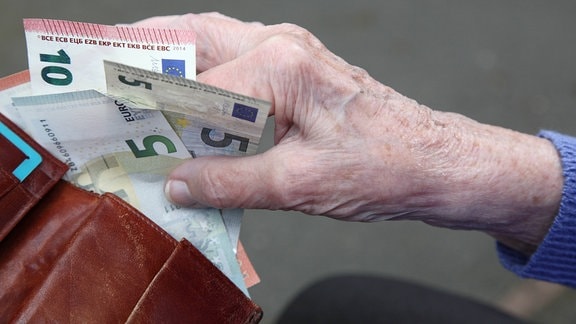 Eine Seniorin haelt Geldscheine in ihrer Hand.