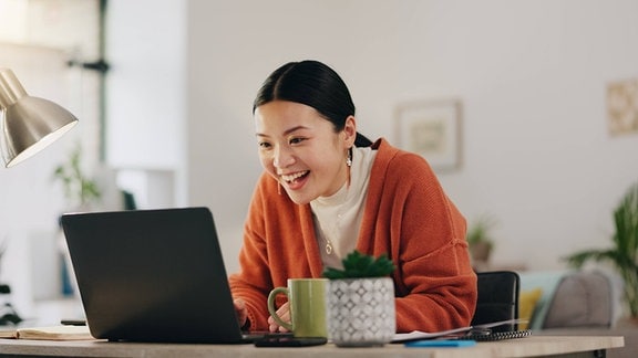 Eine Frau sitzt vor einem Laptop und lacht