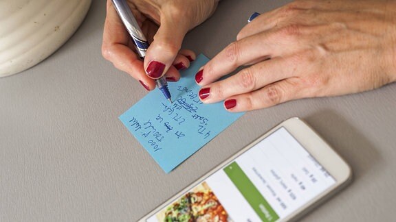 Eine Frau schreibt von einem Smartphone ein Rezept ab