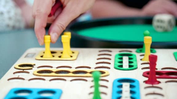 Eine Hand greift eine gelbe Spielfigur eine Brettspiels