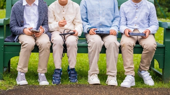 Vier Kinder sitzen auf einer Bank und spielen Computerspiele.