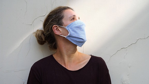 Eine Frau mit Mund-Nasen-Schutz vor einer Wand