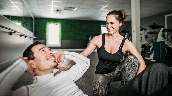 Eine Kraftsport-Trainerin unterstützt einen Mann beim Bauchmuskel-Training