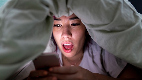 Eine Frau sieht Nachts im Bett auf ihr Handy.