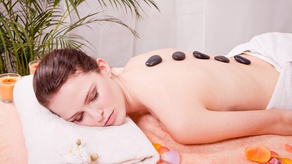 Junge Frau bei einer Wellness-Behandlung mit Steinen auf dem Rücken.