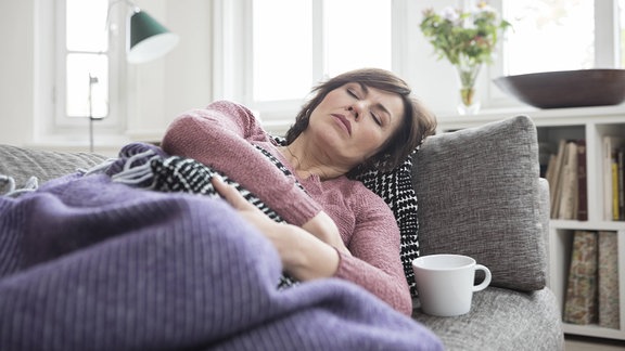 Eine Frau liegt mit Bauchschmerzen auf einem Sofa.