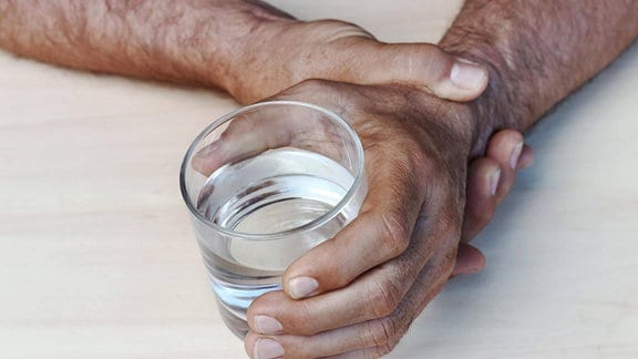 Die Hände eines Mannes mit Parkinson halten ein Wasserglas