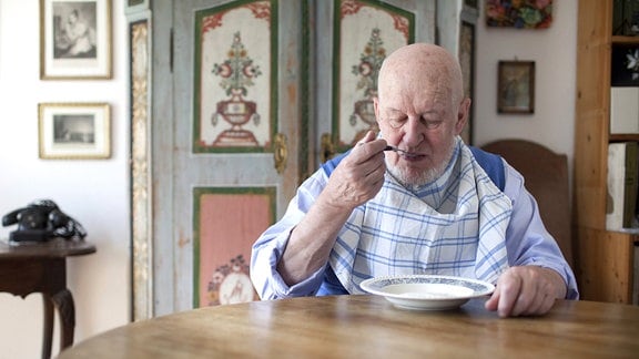 Ein älterer Mann mit Latz am Esstisch