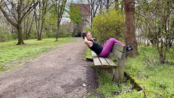 Eine Frau in Sportkleidung sitzt rittlings auf einer Parkbank.