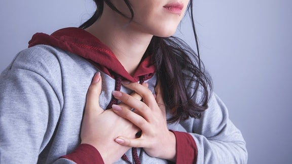 Eine junge Frau drückt ihre Hände auf ihre Brust.