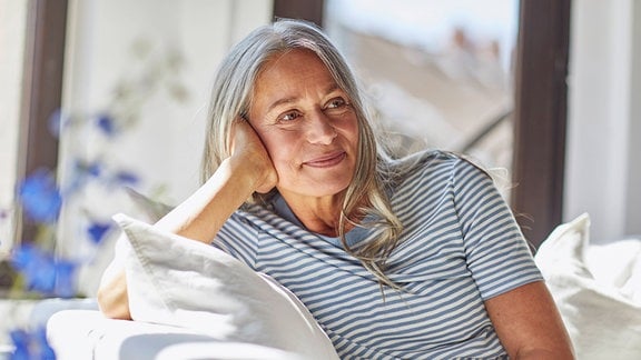 Eine Frau mit langen grauen Haaren sitzt auf einem Sofa.