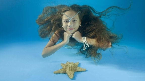 Mädchen mit langen Haaren schaut unter Wasser in die Kamera