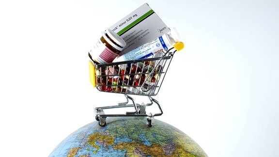 Einkaufswagen gefüllt mit verschiedenen Medikamenten steht auf einem Globus