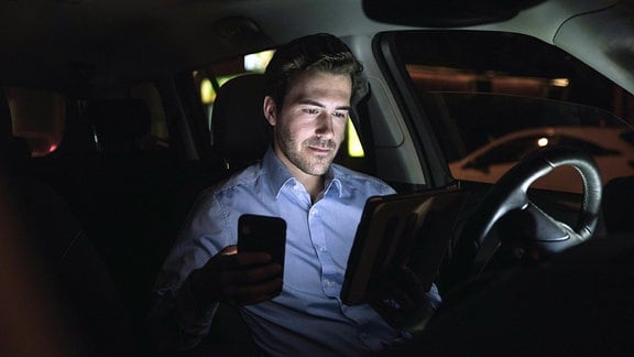 Mann mit Smartphone und Tablet nachts im Auto