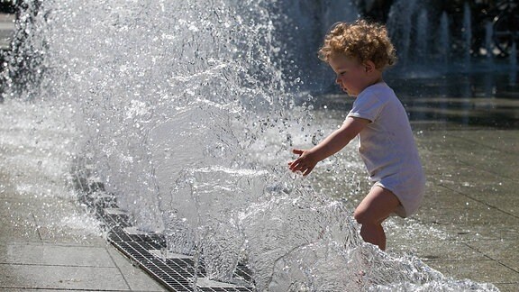 Ein Kleinkind spielt an einem Springbrunnen