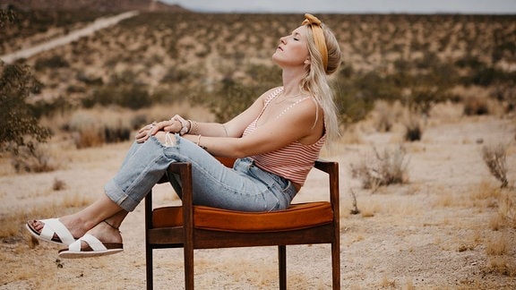 Eine Frau sitzt auf einem Stuhl in einer Wüstenlandschaft