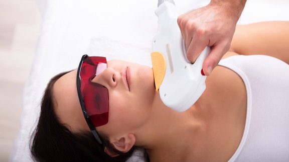 Junge Frau erhält Behandlung mit Lasergerät im Gesicht.