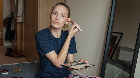 Eine Frau sitzt auf dem Bett und trägt Make-up auf.